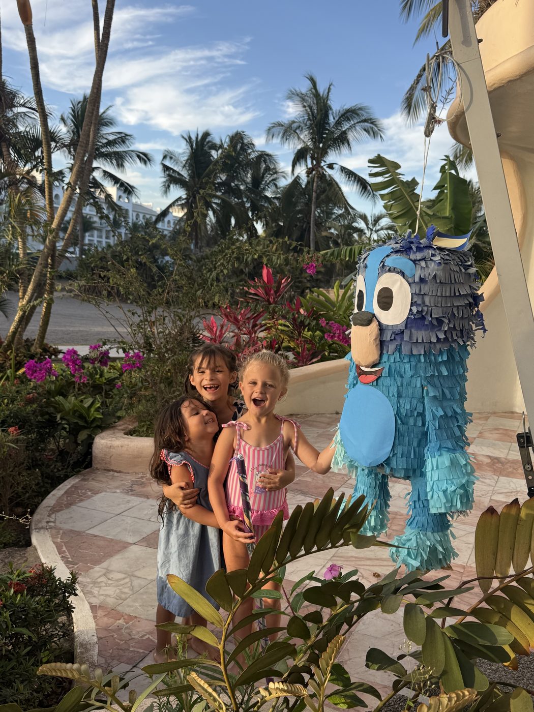 A We Care caregiver and two children at a celebration beside bright bougainvillea