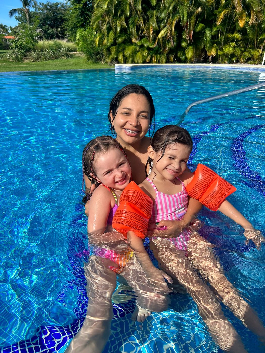 A We Care caregiver and two children holding each other, laughing, in a villa pool