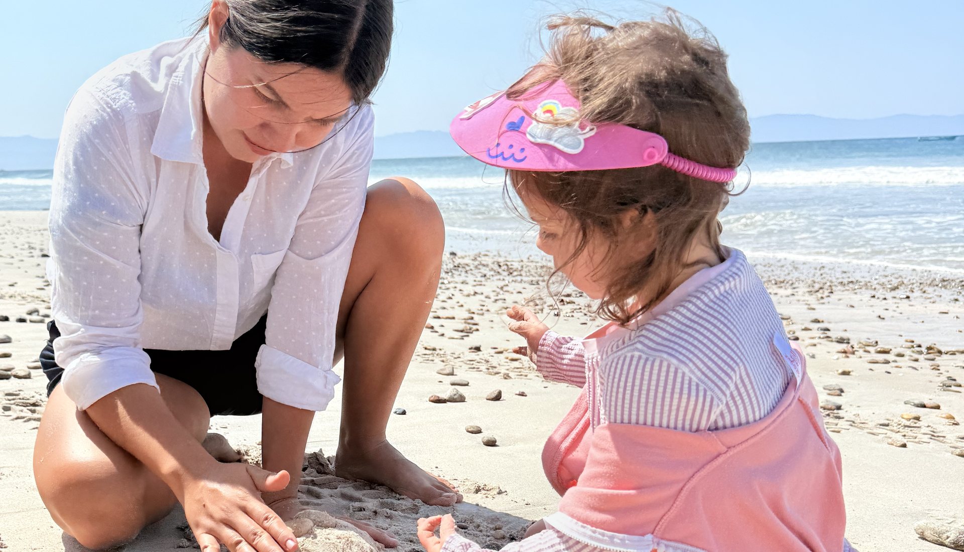 A We Care caregiver crouched beside a young girl, building a sandcastle together on a Punta Mita beach