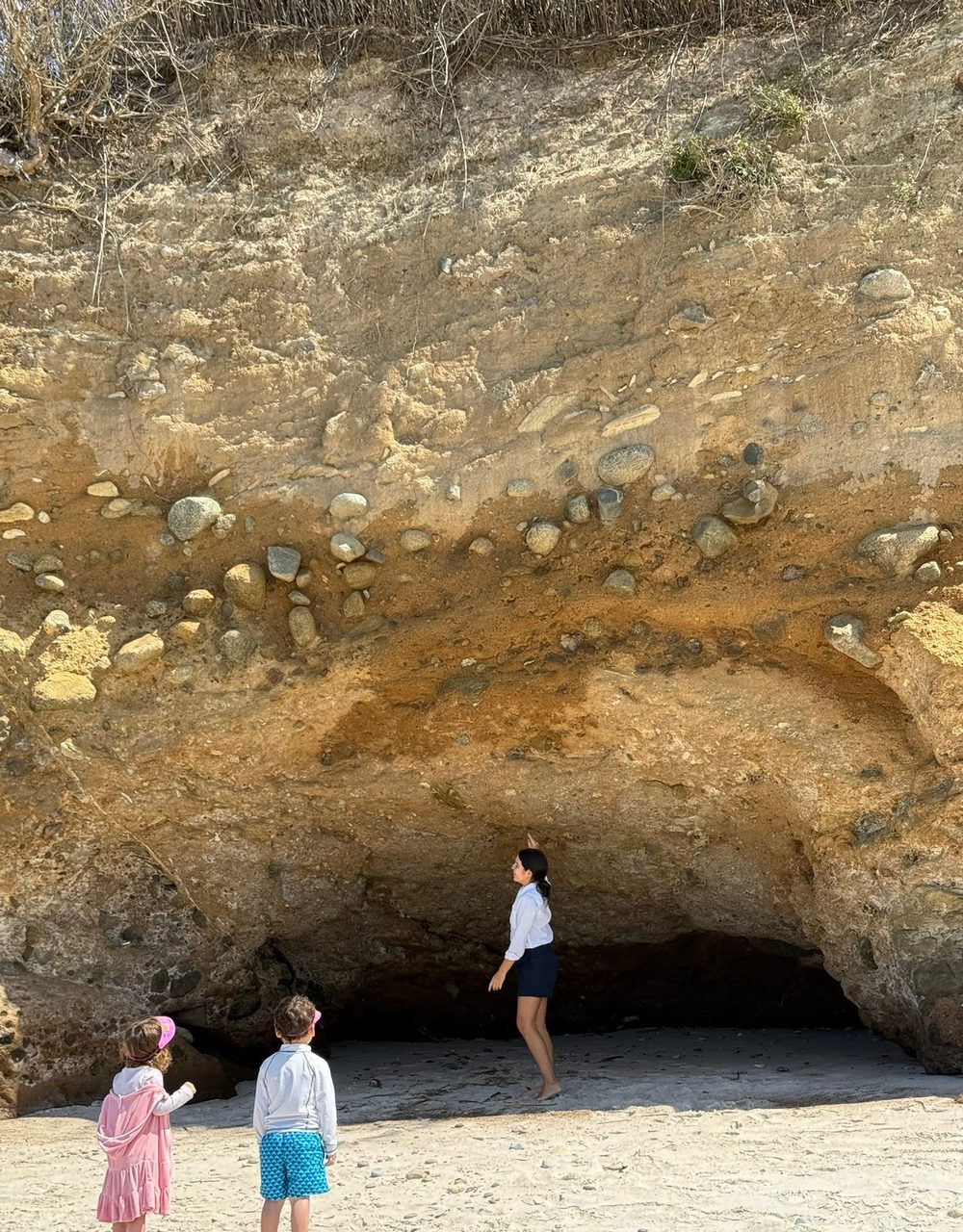 A We Care caregiver and two children exploring a sandstone sea cave on a Punta Mita beach