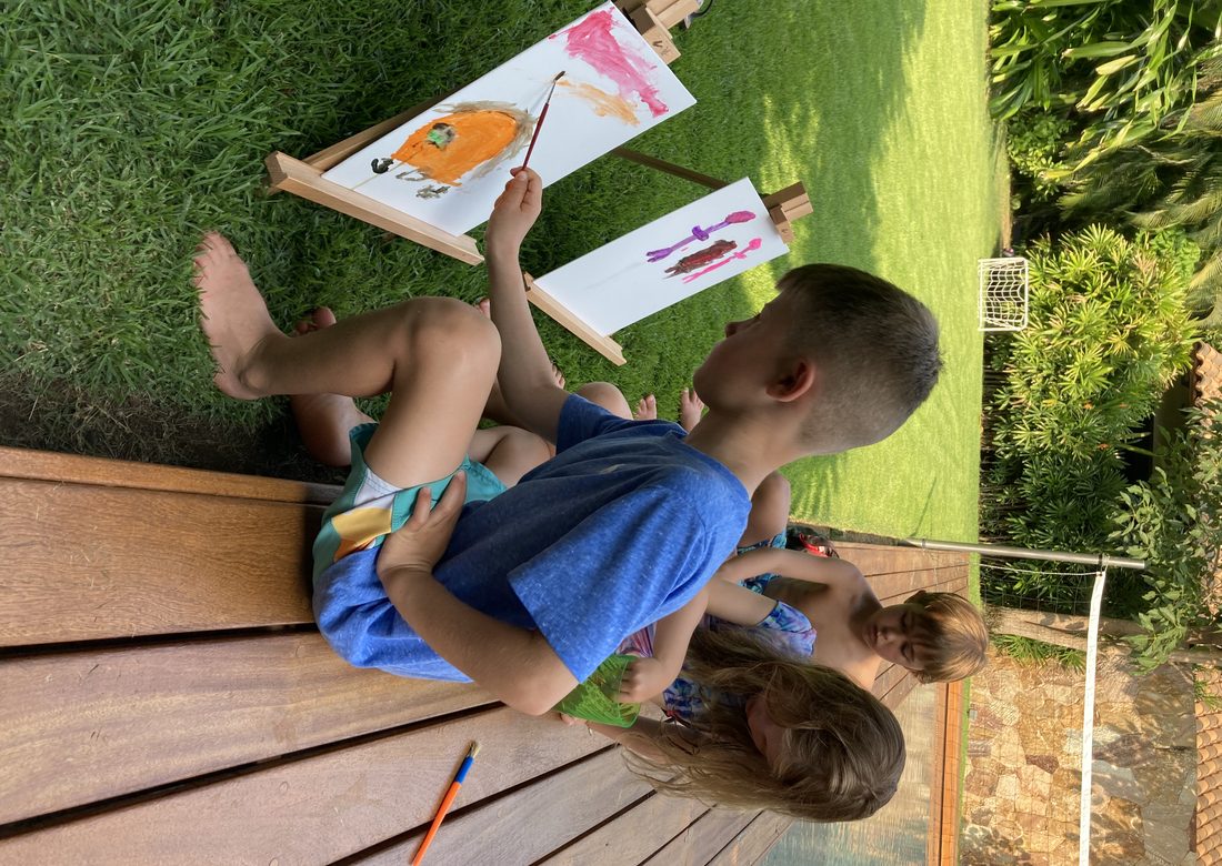 Children painting at wooden easels in a villa garden