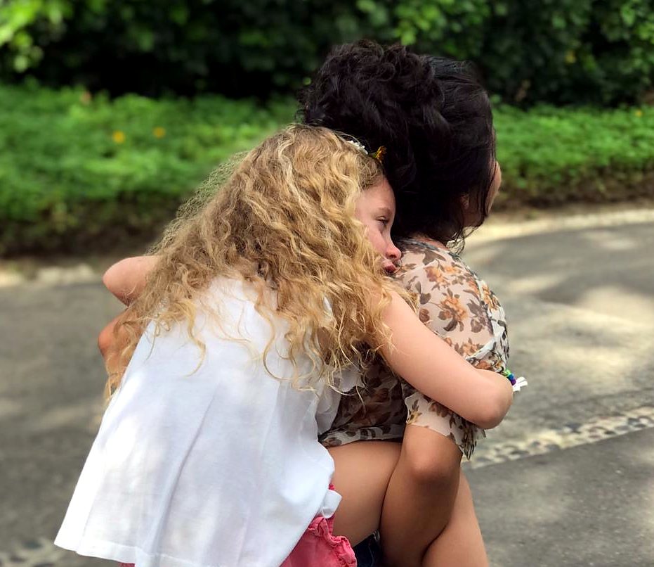 A child from a returning family holding on tightly, carried in the arms of her We Care caregiver