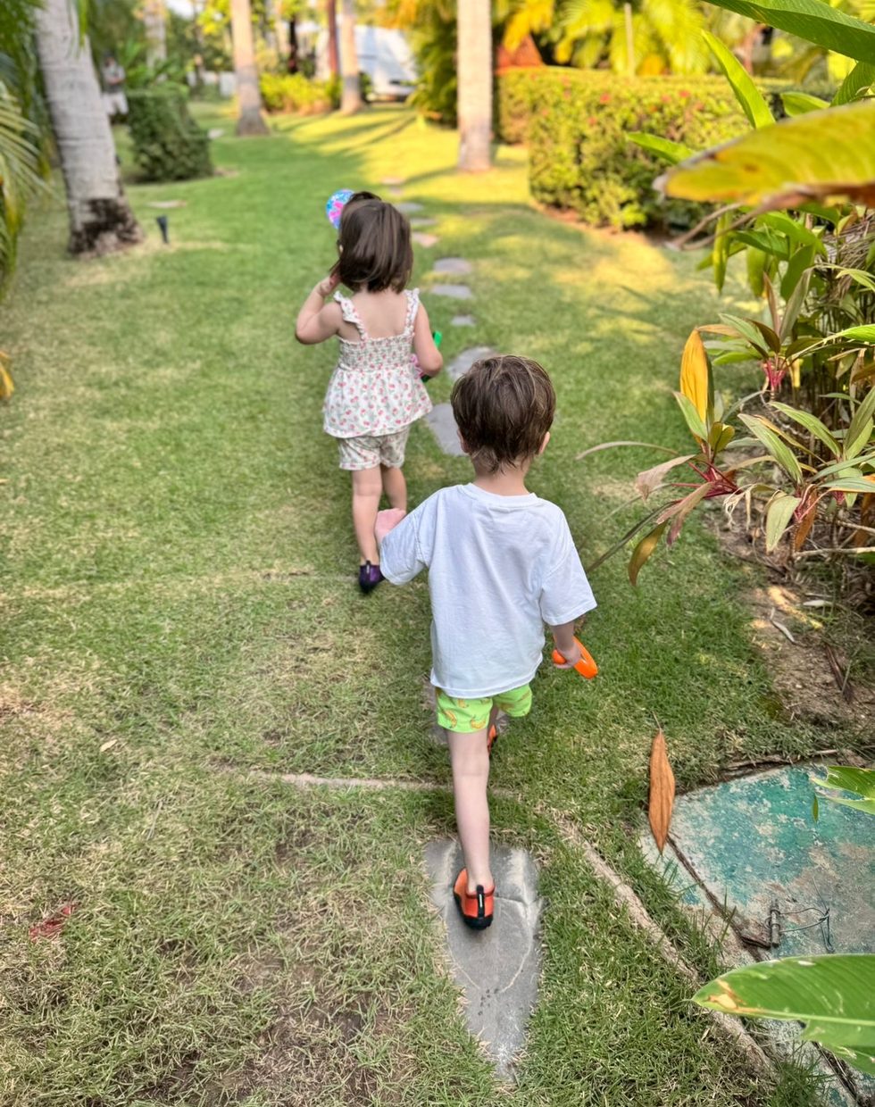 Two children walking a stone path into a lush villa garden in Punta Mita at golden hour
